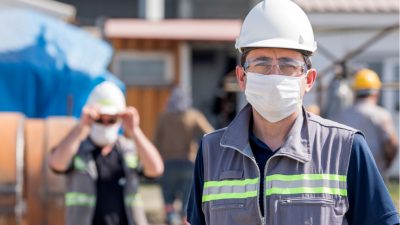 Workers in hard hats and face masks standing in front of a shipping container.